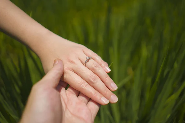 Lamaran pernikahan romantis. tangan dekat dari pasangan dalam cinta memegang erat bersama-sama, wanita dengan cincin pertunangan di jarinya terisolasi di latar belakang lapangan hijau — Stok Foto