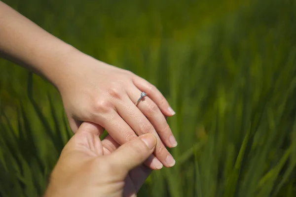 Lamaran pernikahan romantis. tangan dekat dari pasangan dalam cinta memegang erat bersama-sama, wanita dengan cincin pertunangan di jarinya terisolasi di latar belakang lapangan hijau — Stok Foto