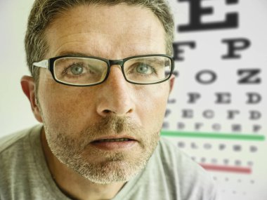 Göz doktorunda gözlük deneyen çekici bir adam. Optik muayene sırasında 40 'lı yaşlardaki bir adam gözlerdeki miyopları düzeltmek için gözlük testi yapıyor.