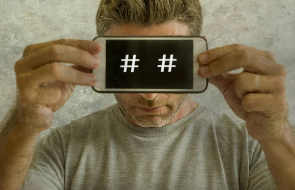 Portrait conceptuel de l'homme accro à Internet et obsédé par l'homme tenant un téléphone portable avec des symboles de hashtag positionnés comme des yeux dans le concept de dépendance aux médias sociaux — Photo