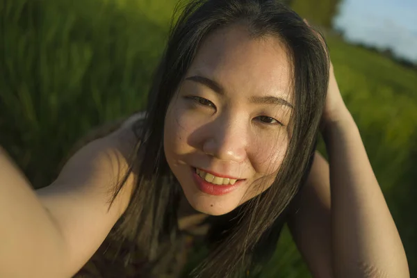 Jeune femme asiatique heureuse et belle prenant selfie photo en plein air. joyeuse fille chinoise en robe d'été prenant autoportrait au champ vert profiter des vacances — Photo