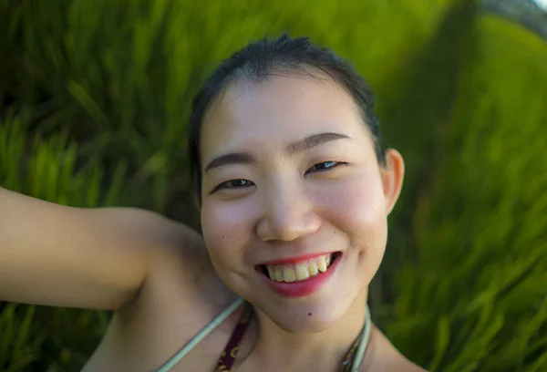 Молодая счастливая и красивая азиатка делает селфи на открытом воздухе. веселая китаянка в летнем платье делает автопортрет на зеленом поле наслаждаясь отпуском — стоковое фото