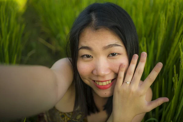 若い幸せと美しいアジアの女性は、彼女の婚約指輪を誇りに屋外で写真を撮る。明るいです中国の女の子として婚約者取ります自己肖像で緑のフィールド — ストック写真
