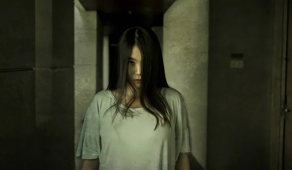 Japanese horror movie style portrait of young strange Asian girl at night in dark solitary hotel corridor looking weird and shady in fear and scary Halloween tribute — Stock Photo, Image