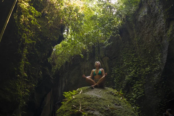 Привлекательная и счастливая средняя взрослая женщина с седыми волосами 40-х или 50-х годов наслаждаясь блаженным и свободным сидением в позе йоги лотоса в красивом зеленом лесу, чувствуя чистоту природы — стоковое фото