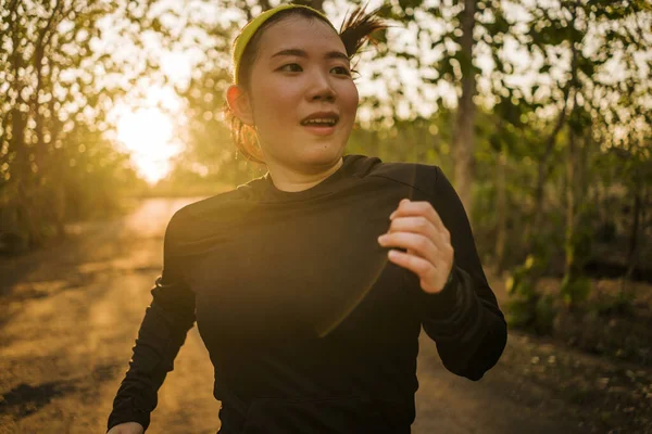 Jovem feliz mulher asiática correndo em madeira no pôr do sol. Menina coreana atraente e saudável fazendo jogging treino na bela estrada rural com árvores no estilo de vida corredor — Fotografia de Stock