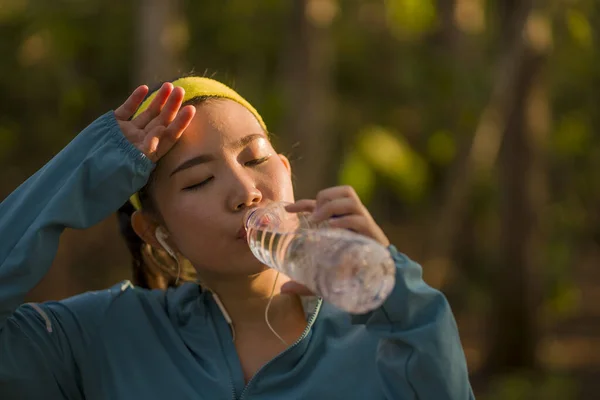 Young Asian runner girl drinking water sweaty and tired. Attractive and exhausted Korean woman thirsty after running workout and jogging at beautiful park — Stock Photo, Image