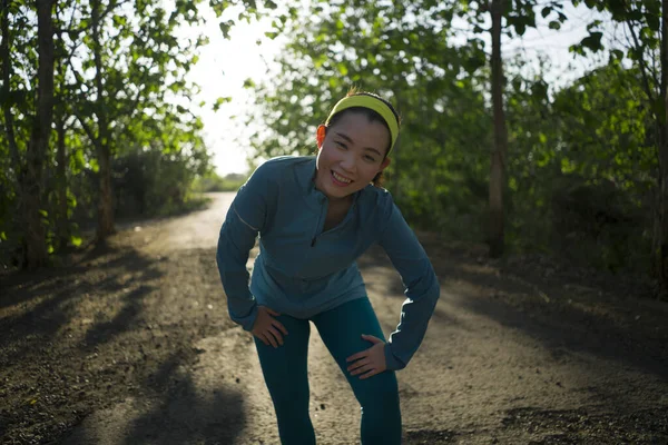 Młoda szczęśliwa Azjatka odpoczywająca podczas treningu w drewnie na zachodzie słońca. Atrakcyjne i zdrowe koreański dziewczyna dysząc po jogging w pięknej wsi drogi — Zdjęcie stockowe