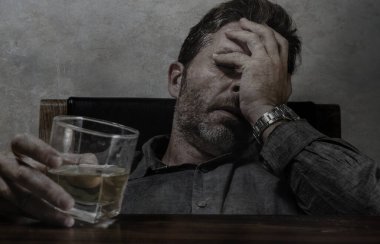 Alkolik ve alkolik bir adam viski bardağının önünde oturmuş alkolizm ve alkol bağımlılığı yüzünden dramatik bir ifadeyle içkiye tutunmaya çalışıyor.
