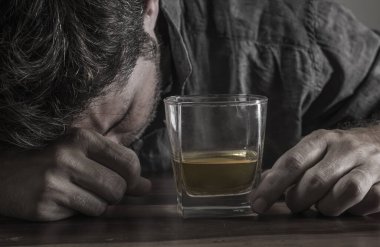 Alkol bağımlılığı ve alkolizm sorununda içki içmenin cazibesine tutunarak 40 'lı yaşlarındaki depresif ve düşünceli alkolik bir adamın viski bardağının önünde sarhoş ve stresli bir şekilde durması.
