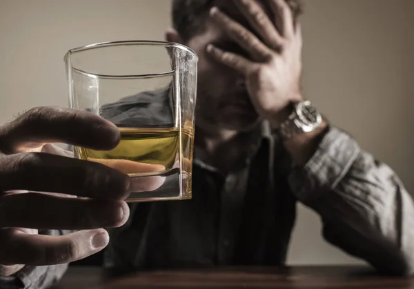 Homme alcoolique déprimé et réfléchi sur sa quarantaine en face de verre de whisky gaspillé et souligné tenant sur la tentation de boire dans la dépendance à l'alcool et le problème de l'alcoolisme — Photo