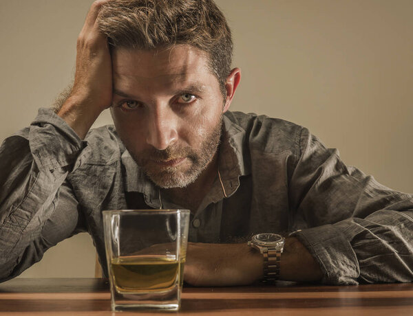 alcoholic depressed and wasted addict man sitting in front of whiskey glass trying holding on drinking in dramatic expression suffering alcoholism and alcohol addiction