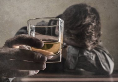 Alkolik ve alkolik bir adam viski bardağının önünde oturmuş dramatik bir ifadeyle içkiye tutunmaya çalışıyor alkolizm ve alkol bağımlılığı çekiyor.