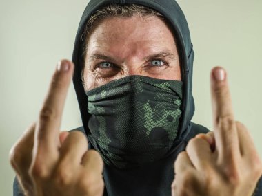 Fanatik ve agresif bir anarşist olan genç adam orta parmağını gösteriyor. Öfkeli ve korkunç anti-sistem protestocusu yüz maskeli isyan sırasında düşmanca bağırıyor.