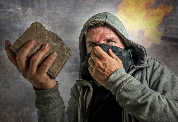 young man as ultra and radical anarchist rioter . furious antifa protester in face mask throwing brick hostile on street on demonstration in violet riot and chaos