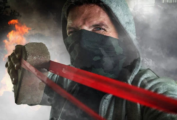 Young man as ultra and radical anarchist rioter . furious antifa protester in face mask throwing brick hostile on street on demonstration in violet riot and chaos — Stock Photo, Image