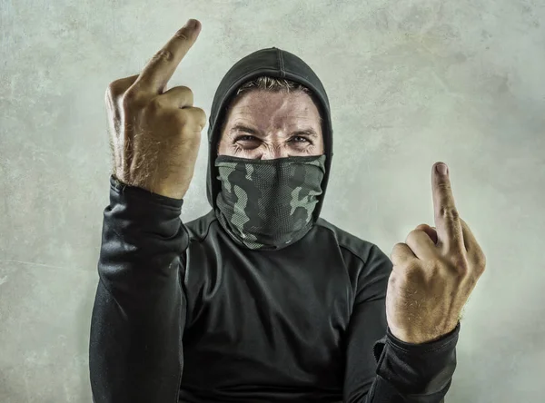 Молодой человек, как фанатик и агрессивный анархист-бунтарь, показывающий средний палец. яростный и страшный яростный антисистемный протестующий в маске для лица кричит враждебно на борьбу с беспорядками — стоковое фото
