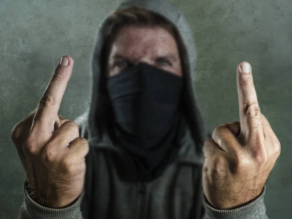 Junger Mann als fanatischer und aggressiver anarchistischer Randalierer, der Mittelfinger zeigt. Wütender und beängstigend gewalttätiger Anti-System-Demonstrant mit Gesichtsmaske, der feindselig auf Krawall schreit — Stockfoto