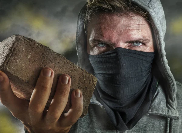 Junger Mann als ultraradikaler anarchistischer Randalierer. Wütender Antifa-Demonstrant mit Gesichtsmaske wirft Ziegelsteine auf Straße bei Demonstration in violettem Aufruhr und Chaos — Stockfoto