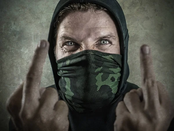 Fanatik ve agresif bir anarşist olan genç adam orta parmağını gösteriyor. Öfkeli ve korkunç anti-sistem protestocusu yüz maskeli isyan sırasında düşmanca bağırıyor. — Stok fotoğraf