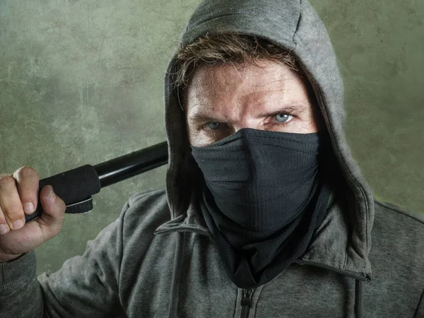 young man as fanatic and aggressive ultra and anarchist rioter . furious anti-system protester in face mask holding baton looking hostile fighting at violent riot