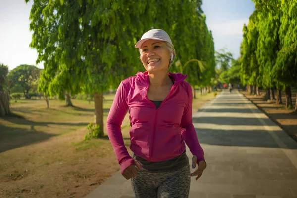 Atraente senhora de meia idade correndo feliz no parque da cidade. mulher bonita e desportiva em seus 40 anos exercitando-se fazendo jogging treino em uma manhã ensolarada desfrutando de um estilo de vida saudável — Fotografia de Stock