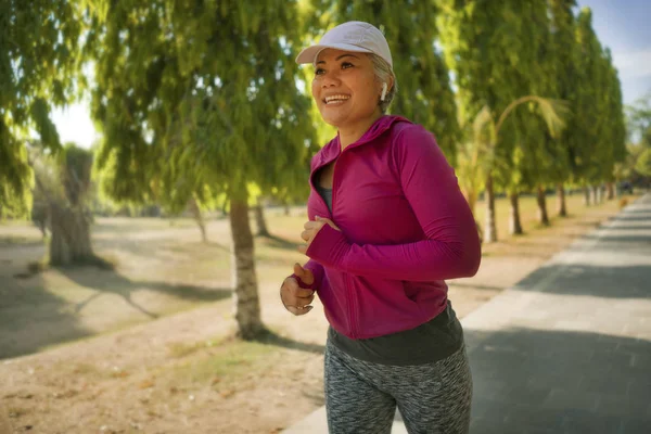 Şehir parkında mutlu koşan orta yaşlı çekici bir bayan. 40 'larında güzel ve sportif bir kadın güneşli bir sabahta egzersiz yapıyor sağlıklı bir yaşam tarzının tadını çıkarıyor. — Stok fotoğraf