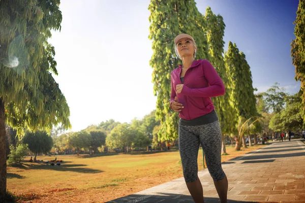 attractive middle aged lady running happy at city park . beautiful and sporty woman on her 40s exercising doing jogging workout on a sunny morning enjoying healthy lifestyle