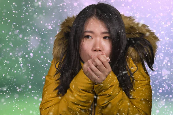 Bela mulher coreana asiática sentindo frio e frio congelamento sentindo frio no inverno vestindo casaco amarelo com capuz de pele esfregando as mãos para se aquecer sob nevasca — Fotografia de Stock