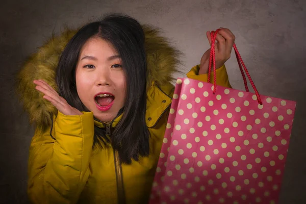 Ung vacker och glad asiatisk koreansk kvinna i cool vinterjacka håller shoppingväska glada köpa julklapp ler glad i mode och skönhet koncept isolerad — Stockfoto