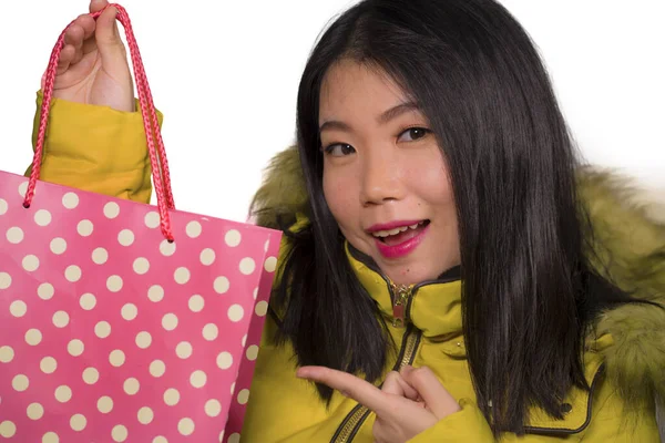 Young beautiful and happy Asian Chinese woman in cool winter jacket holding shopping bag excited buying Christmas present smiling cheerful in fashion and beauty concept isolated — Zdjęcie stockowe