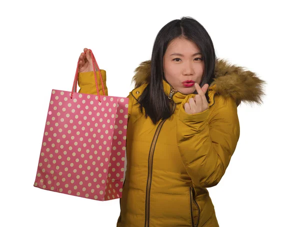 Young beautiful and happy Asian Chinese woman in cool winter jacket holding shopping bag excited buying Christmas present smiling cheerful in fashion and beauty concept isolated — Stockfoto