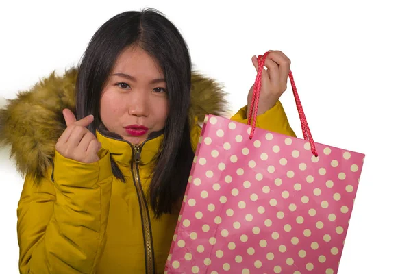 Young beautiful and happy Asian Chinese woman in cool winter jacket holding shopping bag excited buying Christmas present smiling cheerful in fashion and beauty concept isolated — Zdjęcie stockowe