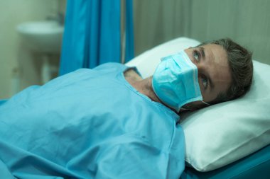 Çekici ve korkmuş bir adam kovid 19 'dan etkilenmiş. Yüz maskesi takmış yetişkin bir erkeğin dramatik portresi hastanede tedavi görüyor. Solunum hastalığından muzdarip. 