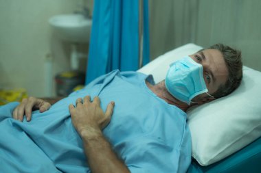 Çekici ve korkmuş bir adam kovid 19 'dan etkilenmiş. Yüz maskesi takmış yetişkin bir erkeğin dramatik portresi hastanede tedavi görüyor. Solunum hastalığından muzdarip. 