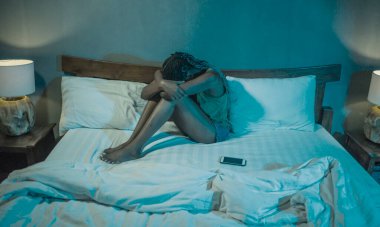 Genç üzgün ve depresif Afrikalı Amerikalı kadının dramatik bir yaşam tarzı portresi. Yatakta cep telefonu zorbalığının ya da yatak odasında kırık bir kalbin kurbanı ile ağlıyor.