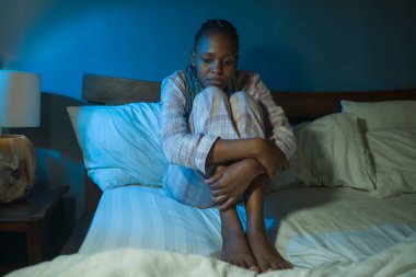Genç üzgün ve bunalımlı siyahi Afrikalı Amerikalı kadın geceleri uykusuz ve endişeli bir şekilde yatağında oturuyor depresyon ve uykusuzluk sorunu yaşıyor.