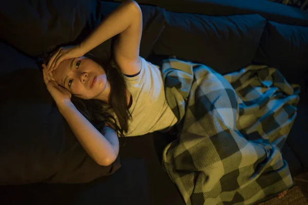 dramatic home lifestyle portrait of young beautiful sad and depressed Asian Chinese woman lying in pain crying at living room sofa couch feeling stressed and worried suffering depression