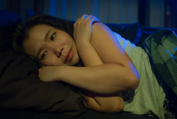 dramatic home lifestyle portrait of young beautiful sad and depressed Asian Korean woman lying in pain at living room sofa couch broken heart suffering depression and anxiety