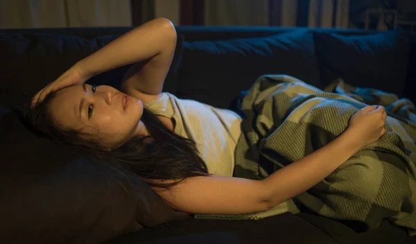 dramatic home lifestyle portrait of young beautiful sad and depressed Asian Korean woman lying in pain at living room sofa couch broken heart suffering depression and anxiety