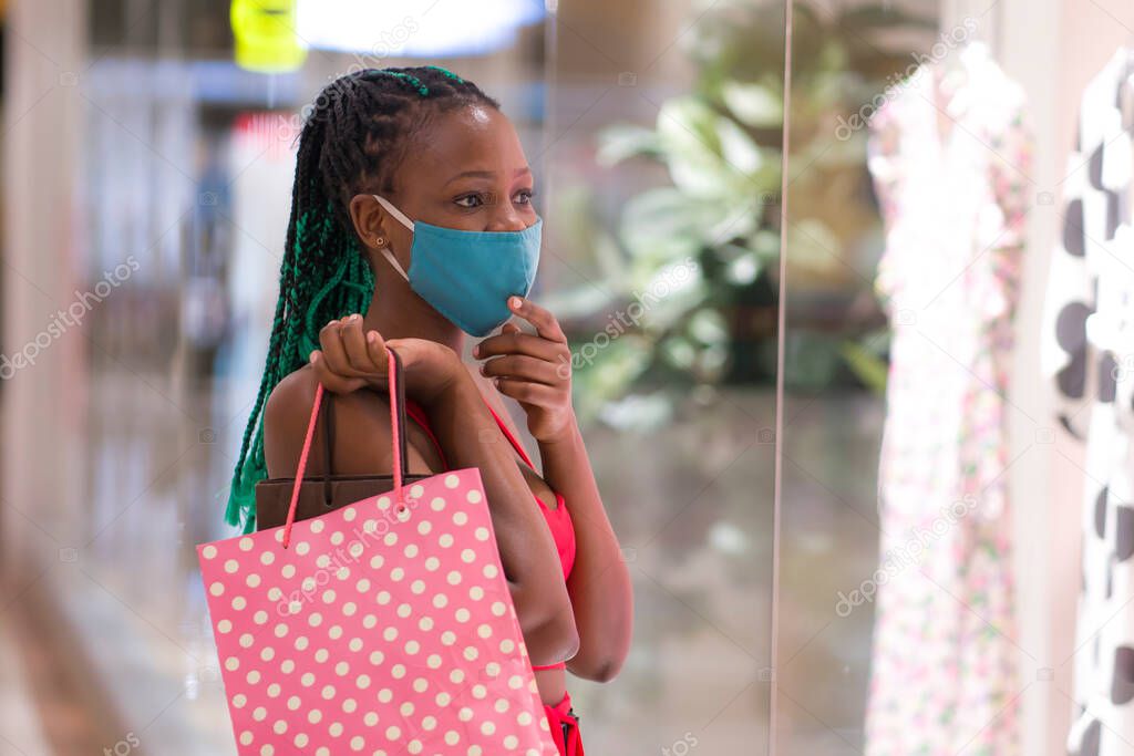 young afro American woman at shopping mall in new normal after covid-19 - happy and beautiful black girl in face mask holding shopping bags enjoying at beauty fashion store 