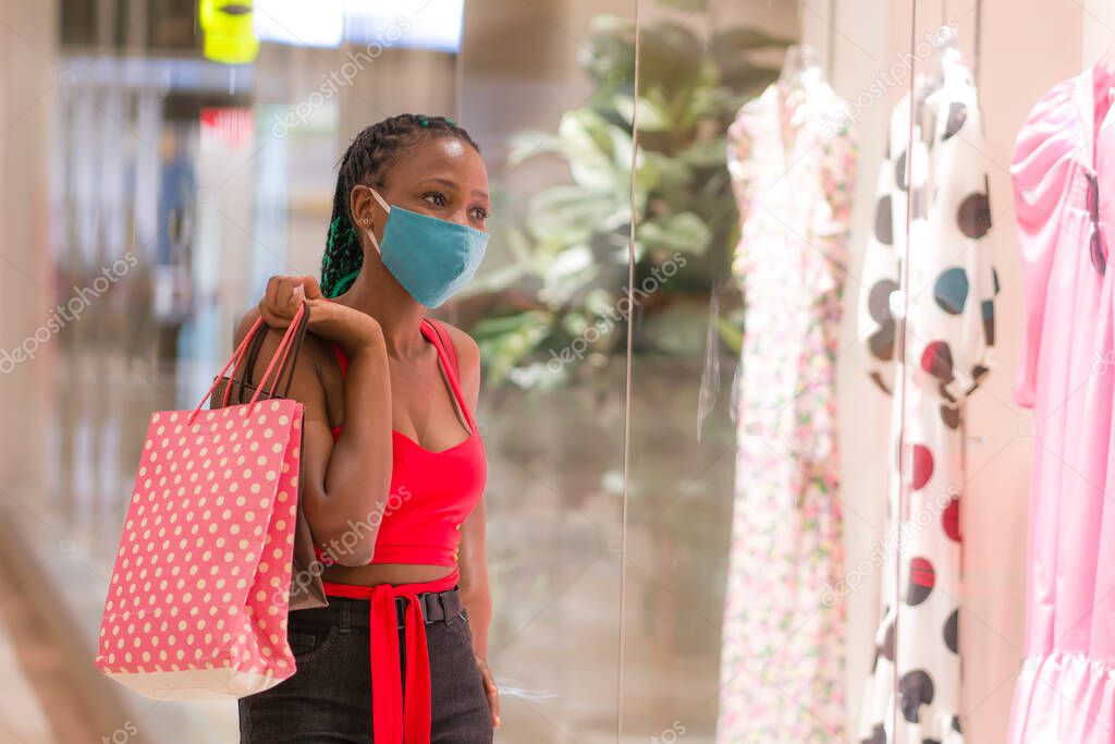 young afro American woman at shopping mall in new normal after covid-19 - happy and beautiful black girl in face mask holding shopping bags enjoying at beauty fashion store 