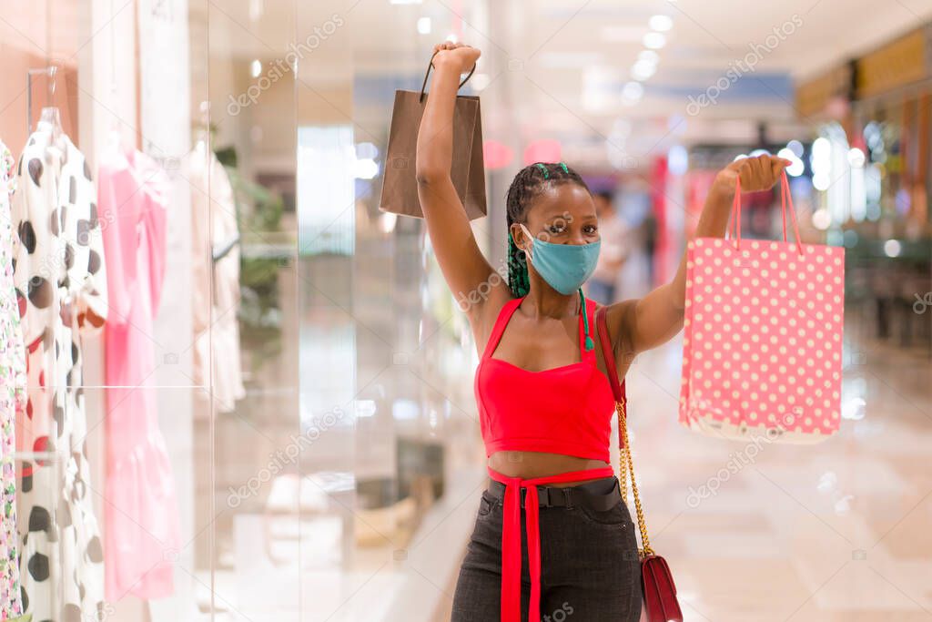 young afro American woman at shopping mall in new normal after covid-19 - happy and beautiful black girl in face mask holding shopping bags enjoying at beauty fashion store 