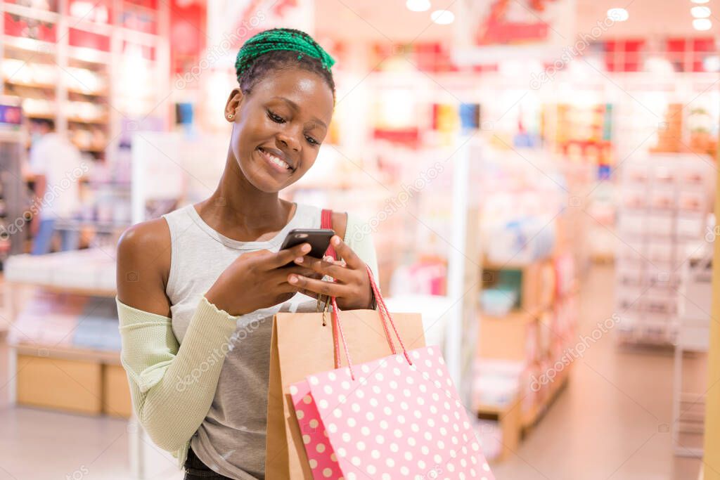 lifestyle portrait of young happy and beautiful black African American woman using mobile phone holding shopping bags buying at mall fashion store smiling cheerful 