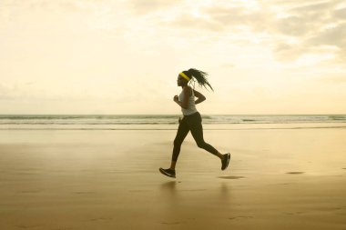 Sahilde koşan Afrikalı Amerikalı bir kadının silueti. Genç, çekici ve atletik bir zenci kız. Açık havada antrenman yapıyor.