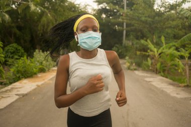 Karantina sonrası koşucu kız dışarıda antrenman yapıyor. Genç, çekici ve formda Afro-Amerikan bir kadın. Yeni normal spor konsepti ve sağlıklı yaşam tarzı ile yüz maskesi takıyor.