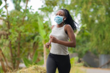 Karantina sonrası koşucu kız dışarıda antreman yapıyor. Genç, çekici ve formda Afro-Amerikan bir kadın. Yeni normal spor konsepti ve sağlıklı yaşam tarzı ile yüz maskesi takıyor.