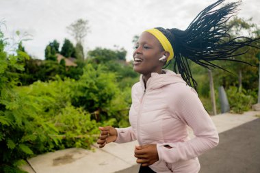 Genç siyahi koşucu kız dışarıda koşmaktan zevk alıyor. Genç, çekici ve formda Afro-Amerikan kadın spor konsepti ve sağlıklı yaşam tarzıyla kırsal yolda koşuyor.