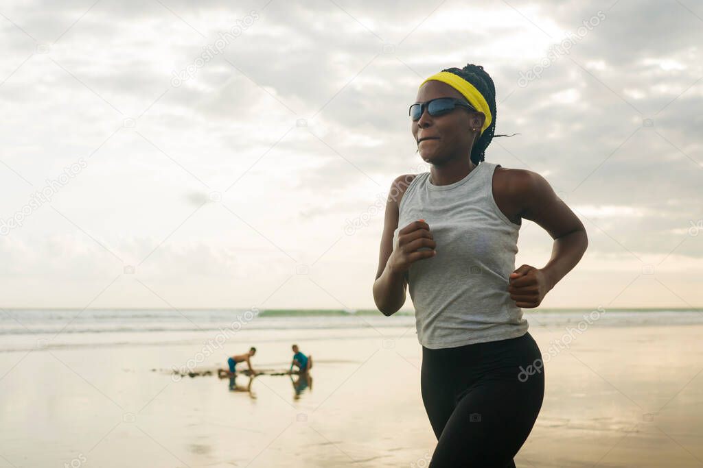 determined African American woman running on the beach - young attractive and athletic black girl training outdoors doing jogging workout at the sea in fitness and healthy lifestyle concept