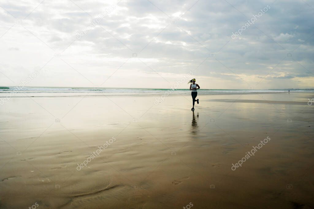 wide lens silhouette of African American runner woman jogging on the beach - young attractive and athletic black girl training outdoors doing running workout at the sea